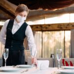 A waiter in a medical protective mask serves the table in the re